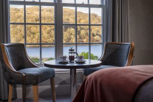 image showing a table and two chairs in front of a window with views of trees and water