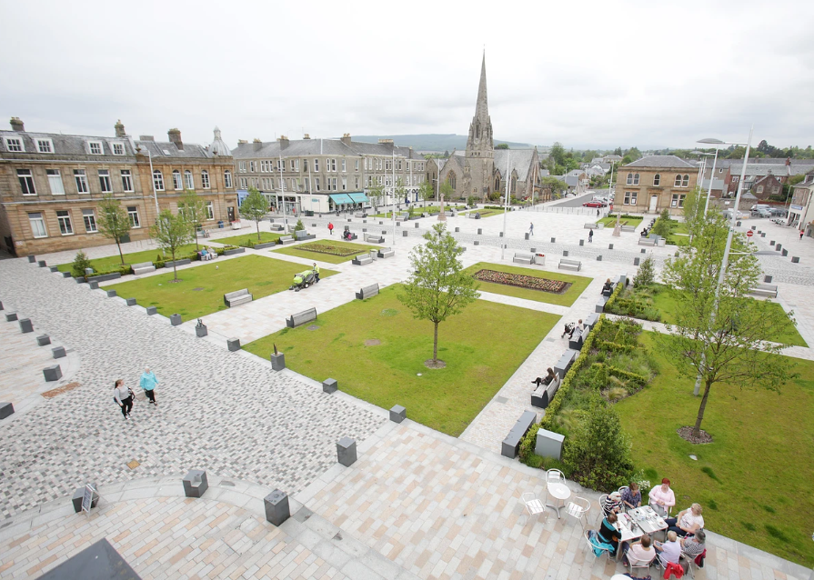 An aerial image of Helensburgh's Colquhoun Square. To the bottom right of the image, a group of people are sitting at a cafe table. 