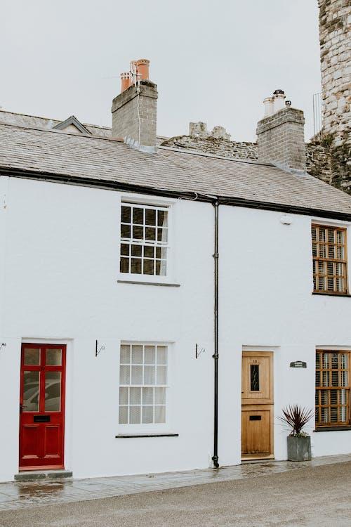 Image shows two white terrace houses next to each other. The house on the left has a red door with two windows above each other. 