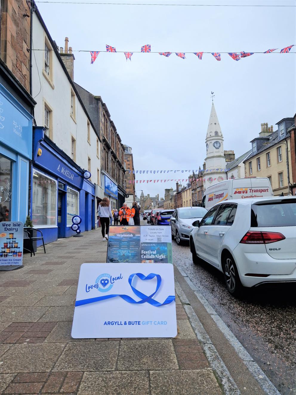 Images shows Campbeltown High Street shops to the left of the picture. Bunting flies above the street and in the foreground is the Argyll and Bute gift card