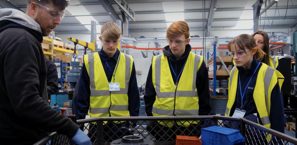 Image shows three young people in hi-vis vests visiting a local business 