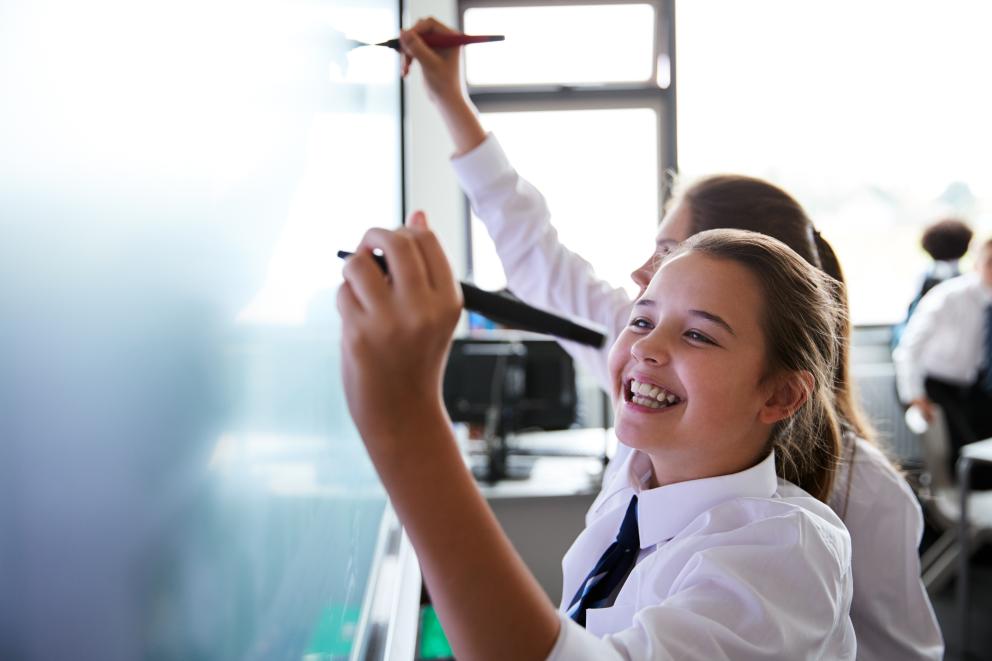 Image shows 2 female pupils writing on a white board 