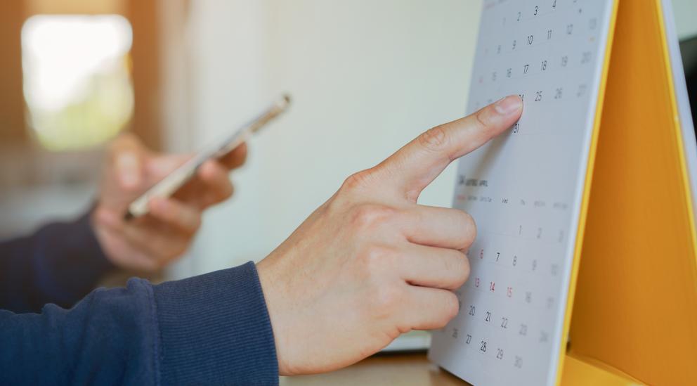 Images shows a calendar with a finger pointing to a date 