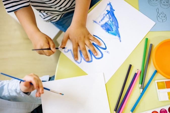 Image shows  child painting around their hand in blue on white paper