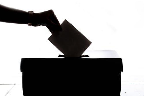 A hand puts a piece of paper into a ballot box
