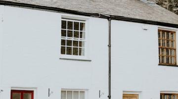 Image shows two white terrace houses next to each other. The house on the left has a red door with two windows above each other. 