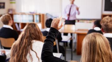 Images shows a class of secondary school pupils at their desks with the teacher at the front of the class. 