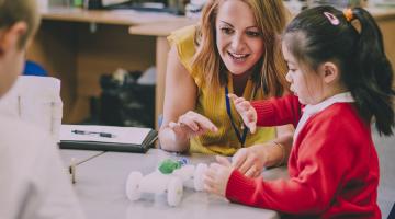 Image shows a young girl sat at a desk with her teacher helping 