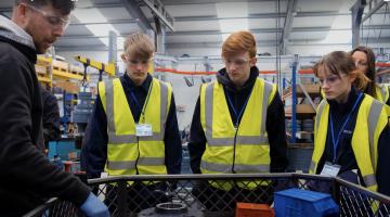 Image shows three young people in hi-vis vests visiting a local business 