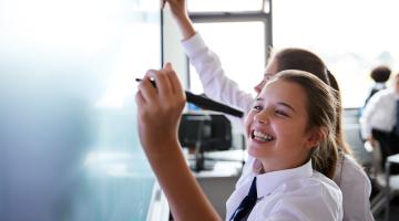 Image shows 2 female pupils writing on a white board 