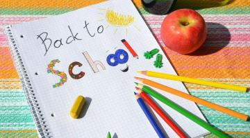 Images shows a notebook with the words back to school with four colour pencils pointing to the words