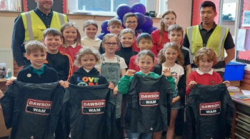 Group of children holding Dawson WAM jackets with workers from Dawson WAM 