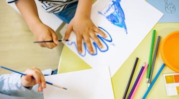 Image shows  child painting around their hand in blue on white paper