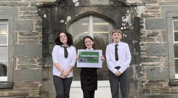 Image shows three children from Colgrain Primary School holding up the Our Children, Their Future strategy