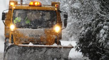 yellow gritter driving through snow with plough attached