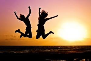 Images shows the silhouette of two young people jumping in the air against a sunset background 