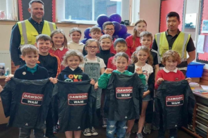 Group of children holding Dawson WAM jackets with workers from Dawson WAM 